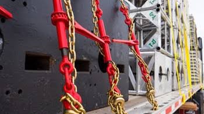 Red load binders and lashing chains securing heavy cargo on a truck bed — OM Enterprise